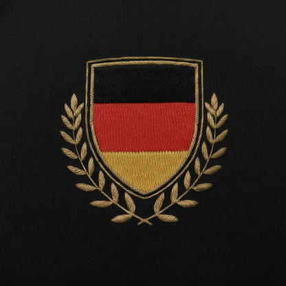 Detailaufnahme der Vorderseite des schwarzen Fan-Polo Deutschland 2026 mit gesticktem Deutschland-Wappen in Schwarz-Rot-Gold und goldenen Ölzweigen